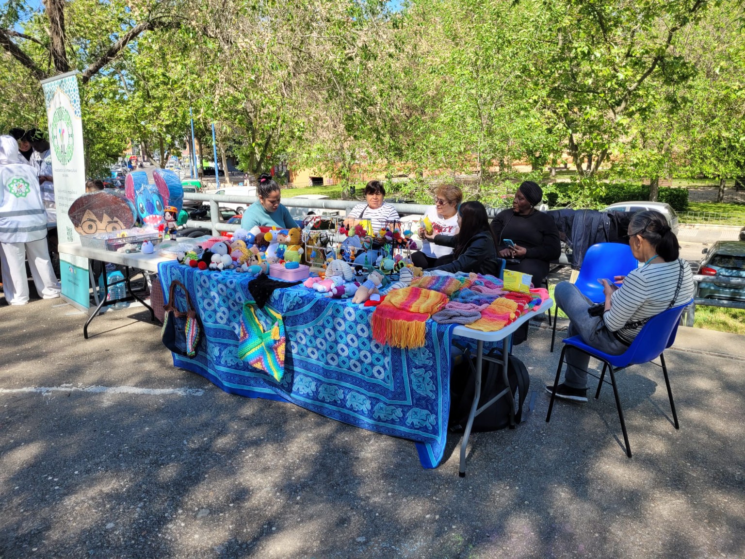 Mesa al aire libre con tejidos y piezas de artesanía y varias personas a su alrededor.