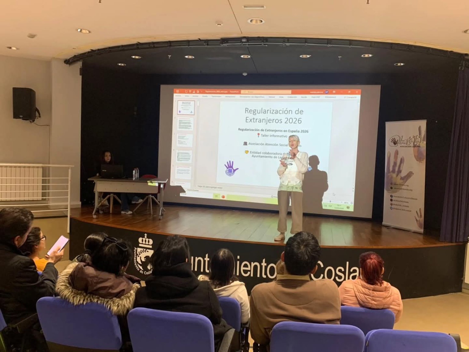 Una ponente presenta una charla informativa en un auditorio con público sentado.